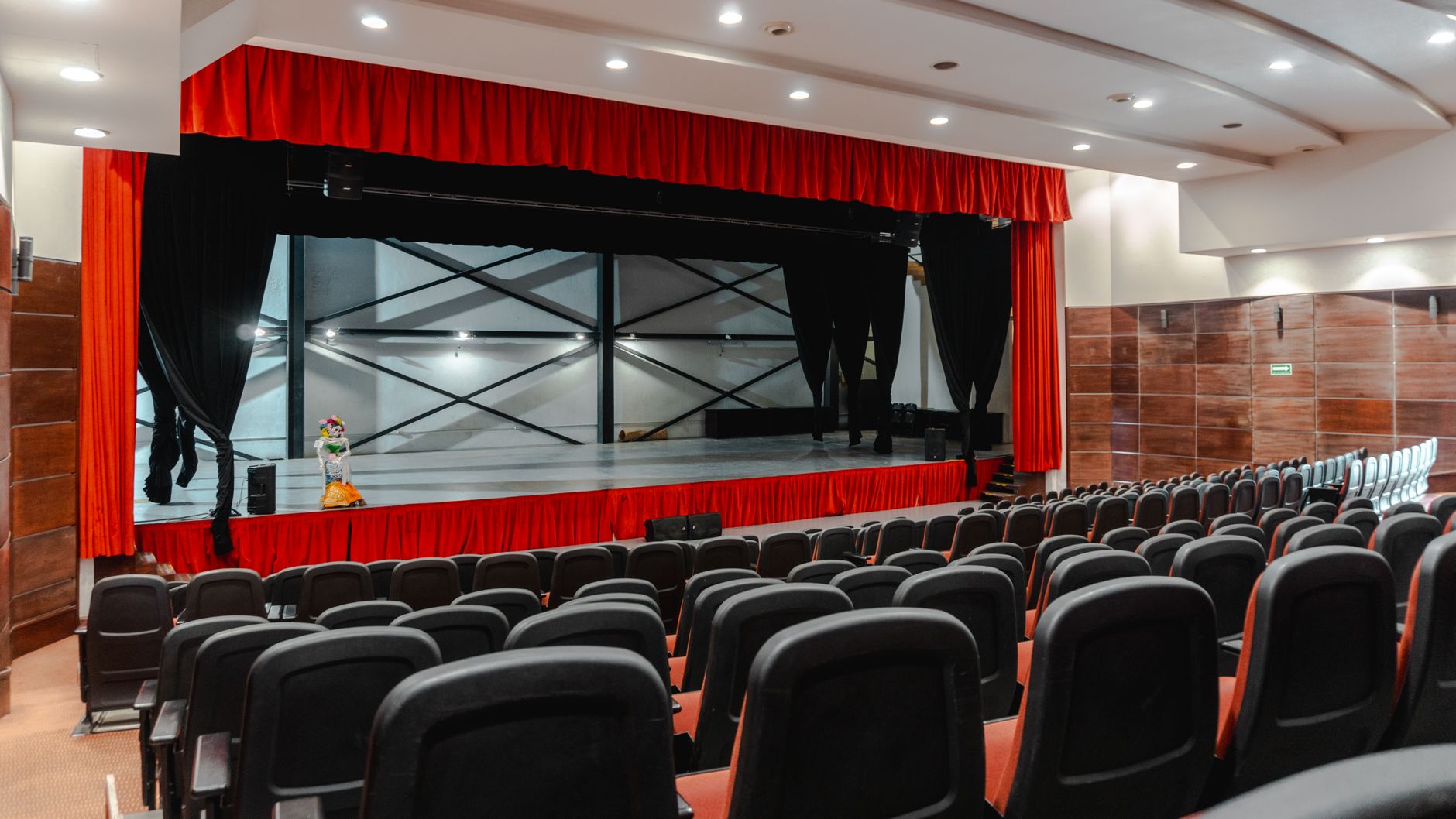 Salle de théâtre vide avec rideaux rouges, rangées de fauteuils face à la scène